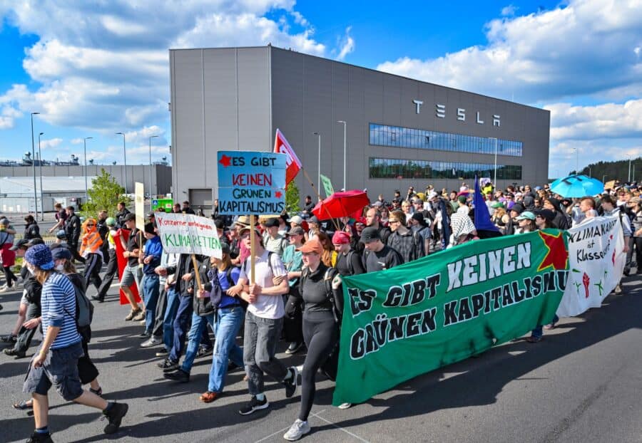 Participanții la un eveniment de protest se îndreaptă spre uzina Tesla. Pe banner se poate citi: "Nu există capitalism verde". Foto Dpa